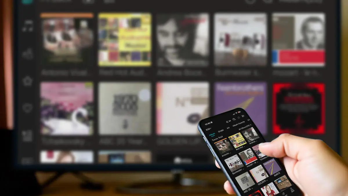 Hand holding smartphone to control eWEAT HiFi Music Streamer via app, with music album covers displayed on a screen in the background - eweat.com